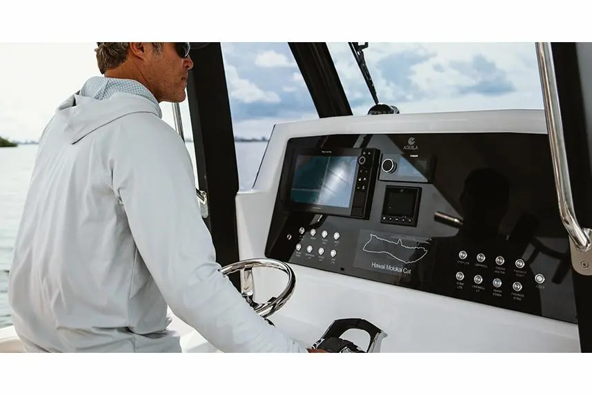 A man wearing a light jacket steers a boat, with a digital control panel displaying marine navigation.